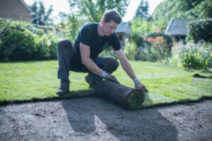 Man rolt graszoden uit op voorbereide grond tijdens het aanleggen van een gazon