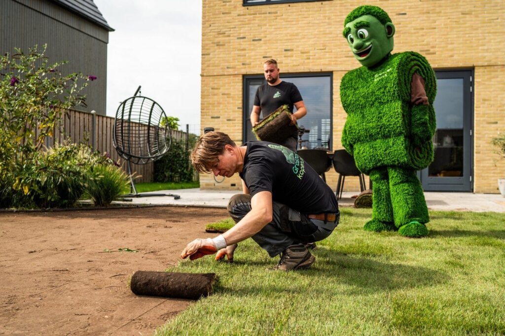 Hovenier legt graszoden langs een houten tuinschutting