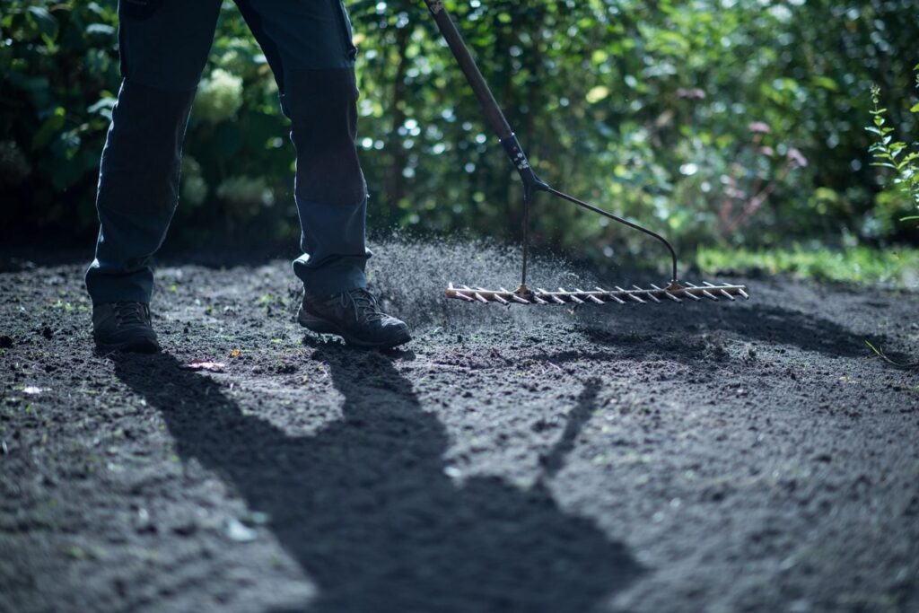 Man harkt droge grond met opwaaiend stofwolkje