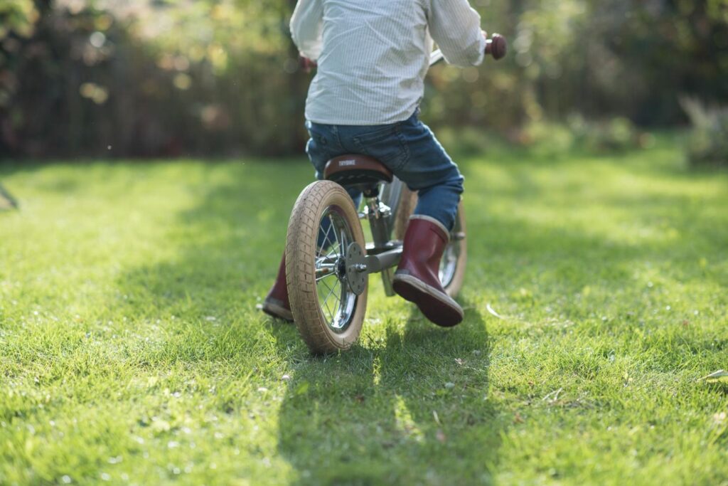 Kind op fiets rijdt over groene graszoden in tuin