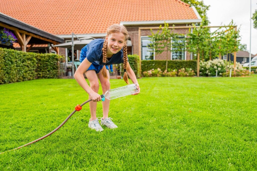 Kind test sproeier van fles en slang op graszoden
