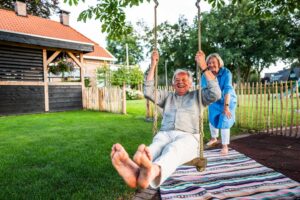 Oudere man schommelt lachend in de tuin met strak groen gazon