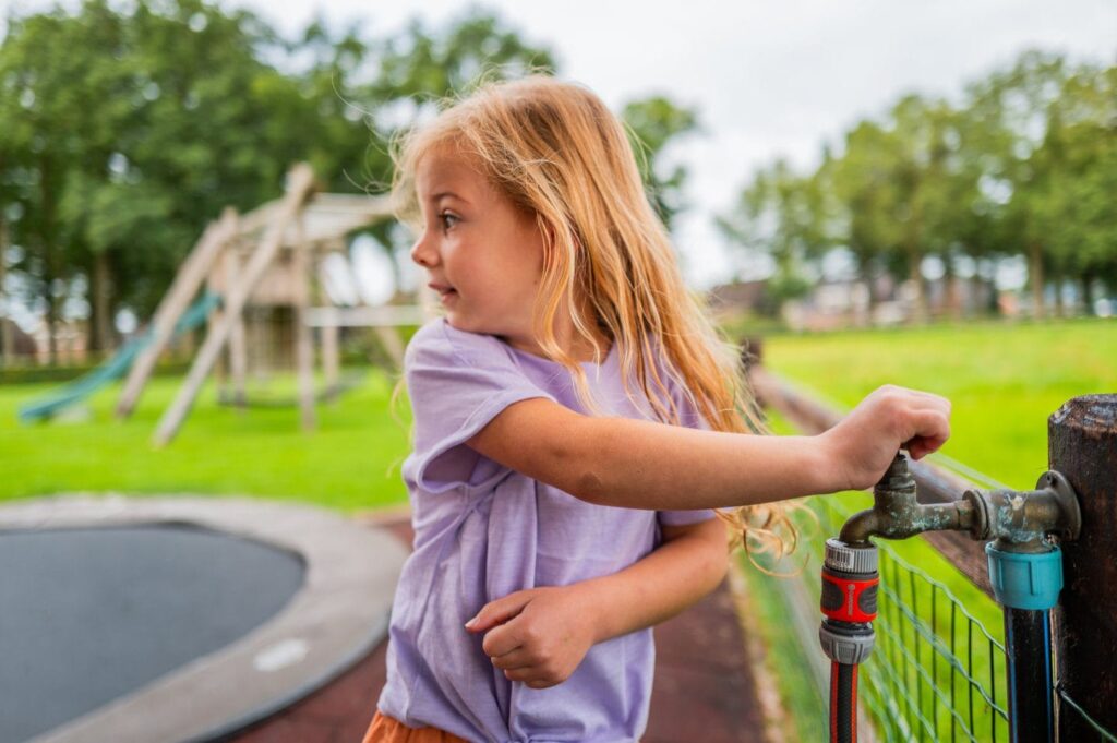 Meisje opent kraan in tuin met trampoline en graszoden