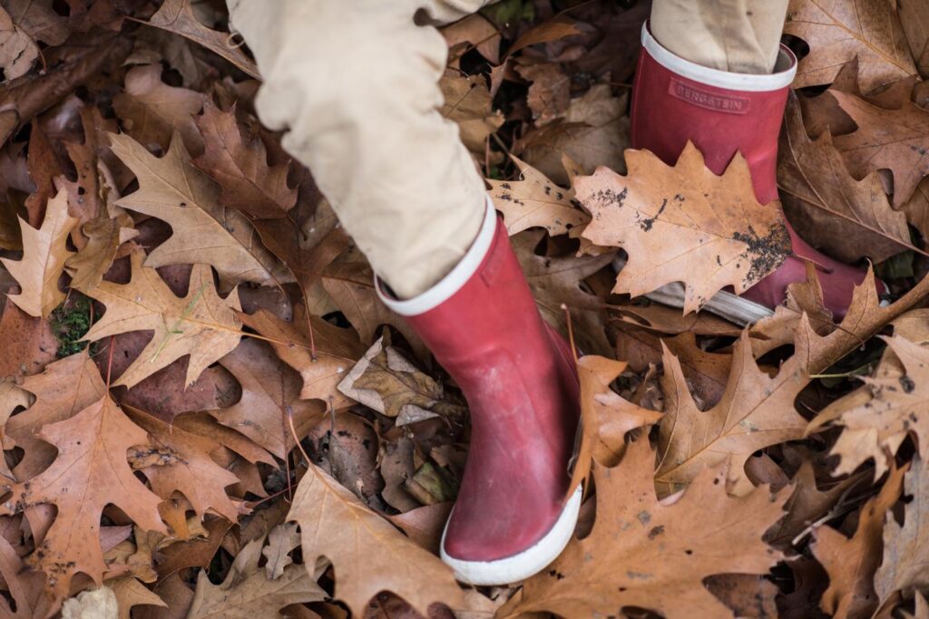 Rode laarsjes tussen herfstbladeren op graszoden
