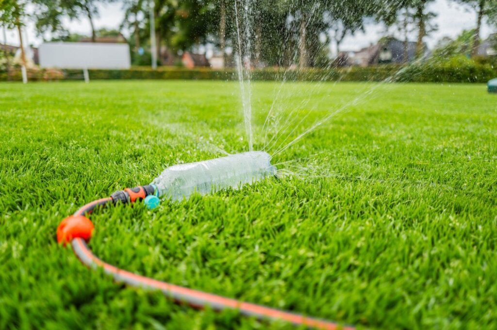 Zelfgemaakte sproeier van een plastic fles op frisgroen gras