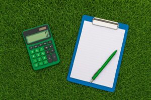 Calculator en kladblok op een groen gazon, symbool voor snel een offerte berekenen voor het laten leggen van graszoden.