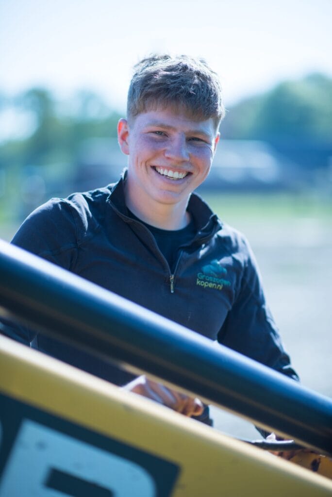 Jonge medewerker van Graszodenkopen.be lachend bij de shovel op het veld