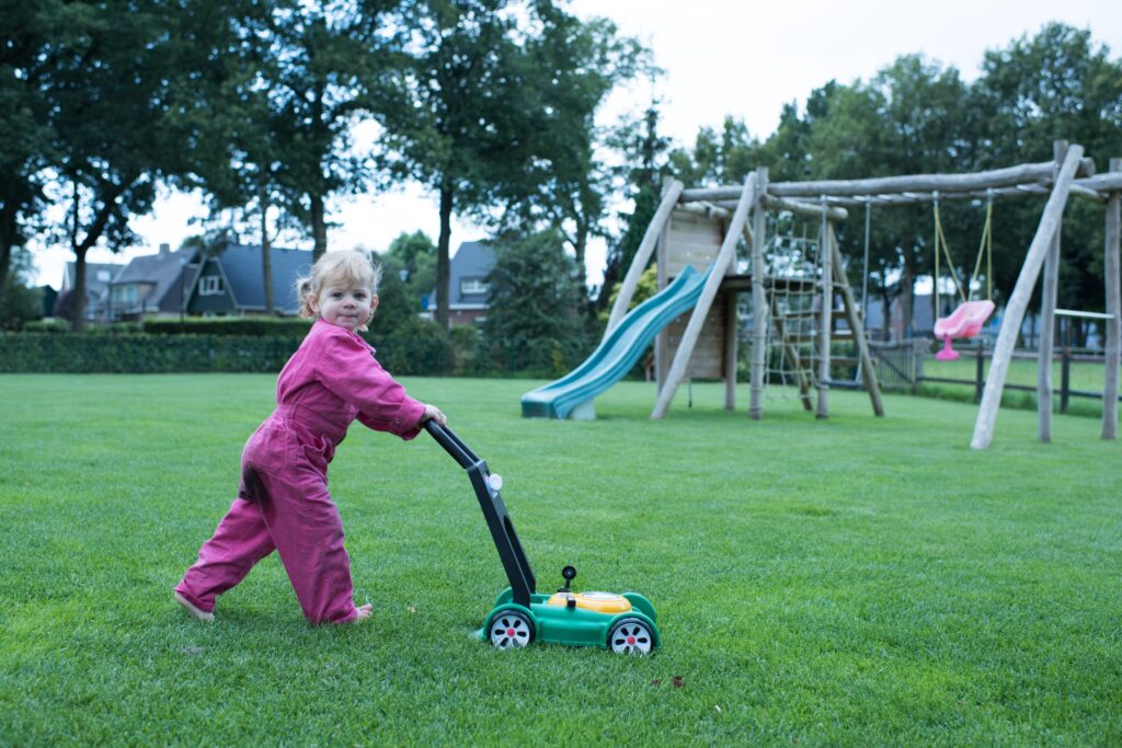 Kind dat met een speelgoedgrasmaaier over een strak groen gazon loopt, symbool voor een veilig en speelklaar grasveld.