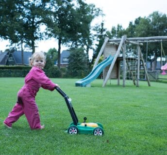 Kind dat met een speelgoedgrasmaaier over een strak groen gazon loopt, symbool voor een veilig en speelklaar grasveld.