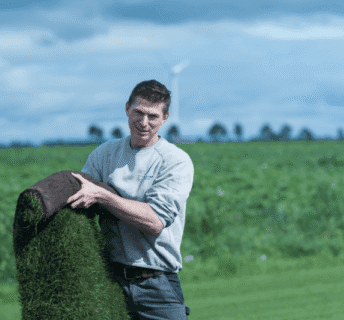 Medewerker van een graszodenbedrijf houdt een rol graszoden vast op het veld