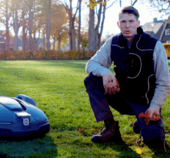 Een gazon in het voorjaar met een robotmaaier waarbij uitleg wordt gegeven door een hovenier